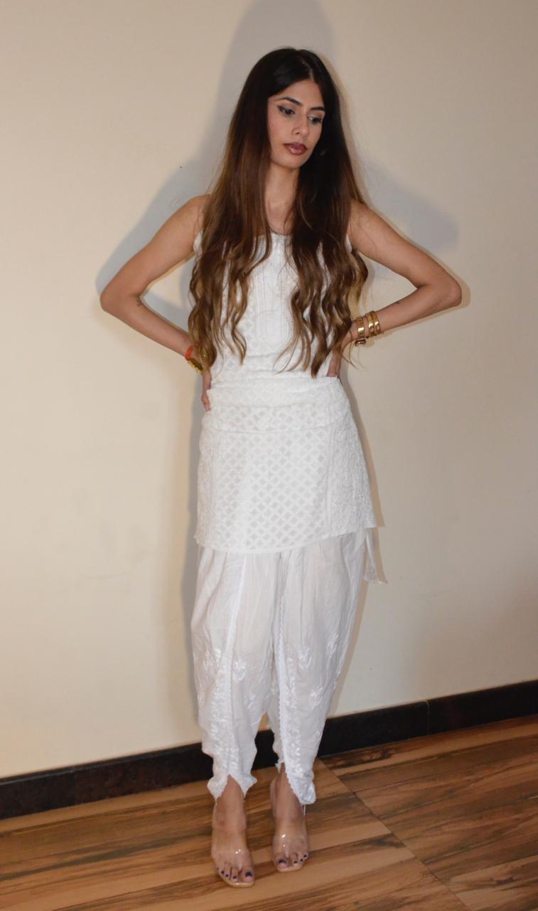 A woman standing, wearing white chikankari dhoti pants with embroidery and a sleeveless top.