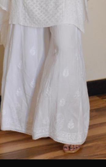Close-up of white palazzo pants with lace detailing and embroidery, showing the texture and pattern.